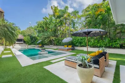 a backyard with a pool and a lawn with chairs and an umbrella at 4BR Villa with Large Pool at Seminyak Beach in Seminyak