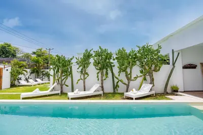a pool with lounge chairs and trees next to a building at Villa Wamwui by DreamAwayBali in Seminyak