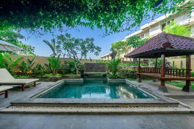 a swimming pool in a garden with a bench and an umbrella at Aradhia Villa Nusa Dua in Nusa Dua