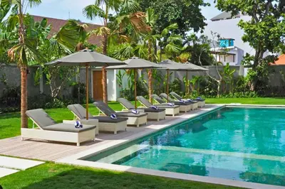 a pool with lounge chairs and umbrellas next to a resort at Narasnama 6 BR Private Pool Villa in Canggu