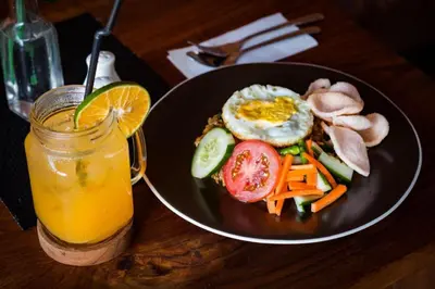a plate of food with an egg and vegetables and a drink at Hadi Poetra Hotel in Kuta