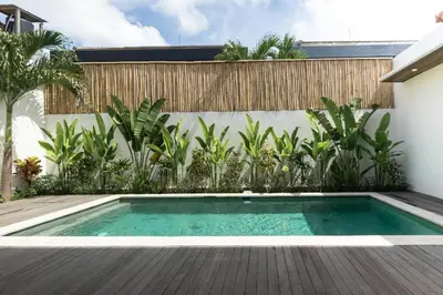 a swimming pool in a backyard with a wooden deck at La Bumbak in Canggu