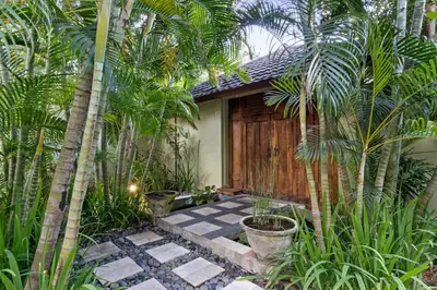 a garden with palm trees and a wooden door at Villa Shantika by Villa Finder in Seminyak