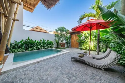 an umbrella and a chair next to a swimming pool at The Secret Jungle Villas Seminyak in Seminyak