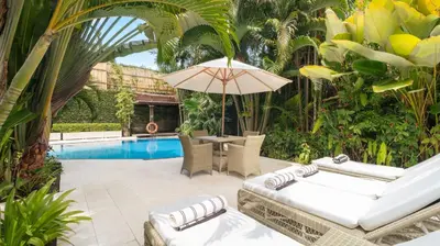 a patio with chairs and an umbrella and a pool at Villa Celeste by Villa Finder in Seminyak