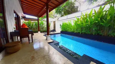 a swimming pool with a table and a chair next to a house at Privat Pool villa at kuta in Kuta