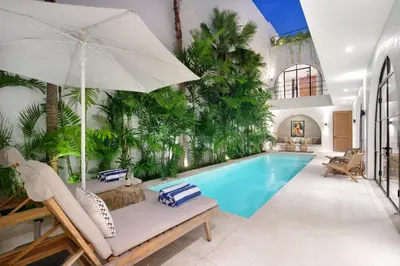 an indoor swimming pool with a white patio furniture and an umbrella at Villa Sugi Umalas in Canggu