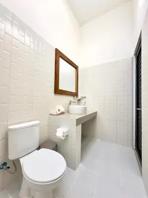 a white bathroom with a toilet and a sink at Bali Stuti Jimbaran Inn in Jimbaran