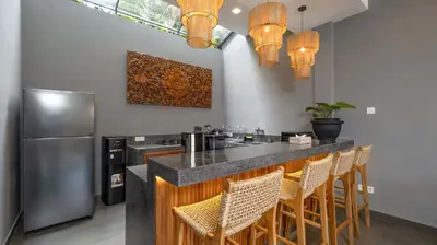 a kitchen with a bar with chairs and a refrigerator at Villa Alami by Villa Finder in Seminyak