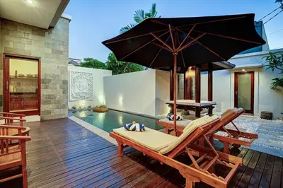 a villa with a pool and a patio with a chair and an umbrella at Villa bella wilson II in Seminyak