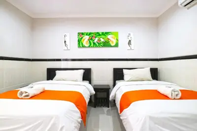two beds in a room with white and orange sheets at Rena Segara House Kuta in Kuta