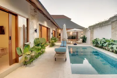 a pool with a chair and an umbrella next to a house at Villa Mayo in Legian