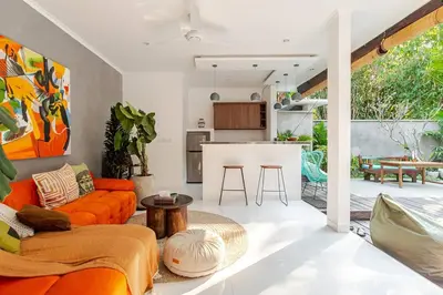 a living room with an orange couch and a kitchen at Villa Aliran - Modern Comfort in tranquil Umalas in Canggu