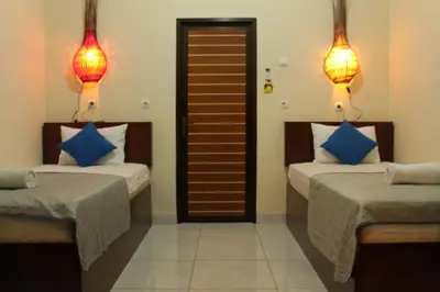 two beds in a room with two lamps on the wall at Chillin Kuta Homestay in Kuta