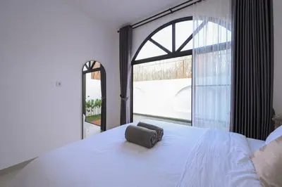 a bedroom with a white bed and a large window at Eunoia Villa in Jimbaran