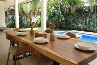 a wooden table with vases and chairs and a pool at Uma dharma villas in Seminyak