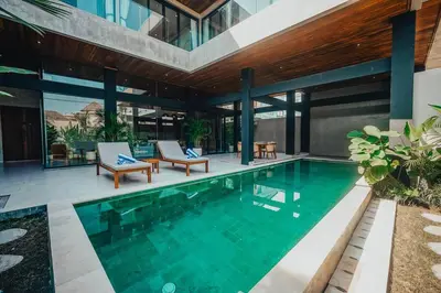 an indoor swimming pool with two chairs and a house at Villa Cintamu - Modern Spacious Villa in Prime Berawa Location in Canggu
