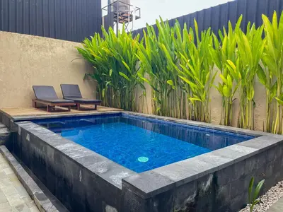 a swimming pool in the middle of a patio with two chairs at Rumah Kodel in Legian in Seminyak