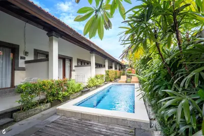 a swimming pool in front of a house with plants at Ayu Guest House 2 in Canggu