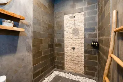 a bathroom with a shower with a stone wall at Vajrayana - 10 Min From The Beach, Serene Villa with Pool View in Kerobokan