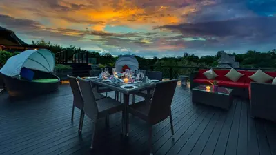 a table and chairs on a deck with a sunset at Villa Aiko in Jimbaran