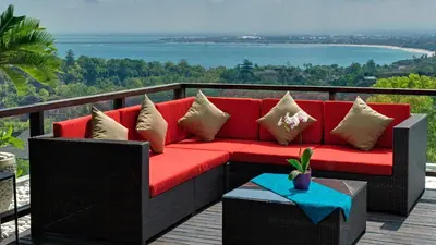 a red couch on a deck with a view of the water at Villa Aiko in Jimbaran