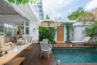 an outdoor patio with a pool and chairs and an umbrella at Casa Elias Seminyak in Seminyak