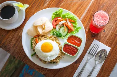 a plate of food with an egg and vegetables on a table at Paras Paros Marina Lodge in Sanur