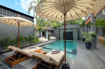 an outdoor patio with a swimming pool and two umbrellas at Alarte Estate by Villa Finder in Seminyak