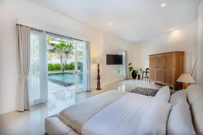 a white bedroom with a large bed and a sliding glass door at Villa Kamboja 1 Seminyak in Seminyak
