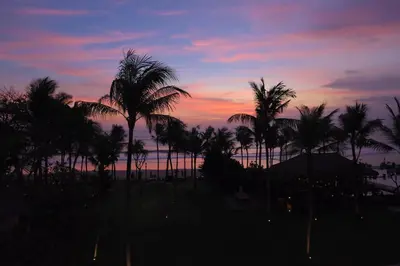 a sunset with palm trees in front of the ocean at 1BR Suite Ocean View in Seminyak