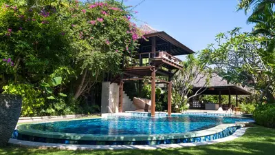a resort pool with a tree house in the background at Villa Asta in Seminyak