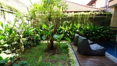 a garden with a tree and a swimming pool at BAGUS Guest House in Legian