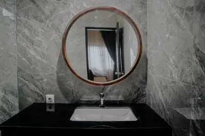 a bathroom with a sink and a round mirror at Shira House Bali in Legian