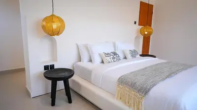 a white bedroom with a bed and a stool at Miko Villa Seminyak in Seminyak