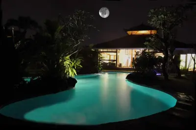a swimming pool at night with the moon in the background at Villa Kija in Seminyak
