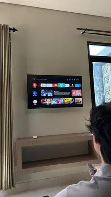 a person sitting on a bench with a television on a wall at Nawasena Suites in Sanur