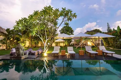 a pool with chairs and umbrellas next to a house at Palm Merah Villa in Umalas