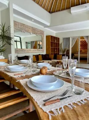 a wooden table with plates and glasses on it at Tranquil Family Villa Retreat in Umalas in Kerobokan
