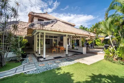 a villa with a thatched roof and a patio at Villa Nyumpene in Legian in Legian