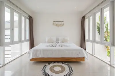 a white bedroom with a bed and large windows at Volare villa in Seminyak