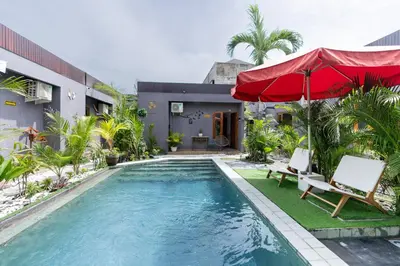 a pool with a red umbrella and chairs and a house at Griya Sadhana Dewi Sri in Legian