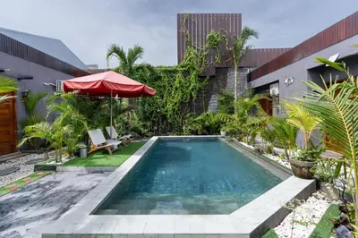 a swimming pool in a garden with a red umbrella at Griya Sadhana Dewi Sri in Legian