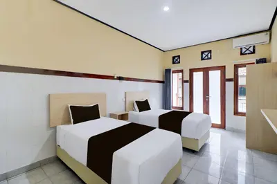two beds in a room with two windows at Townhouse Oak Legian Near Legian Beach Formerly Sayang Maha Merta in Legian