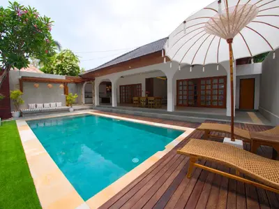 a swimming pool with an umbrella next to a house at Near Beach Villa in Seminyak