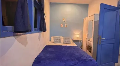a small room with a bed with a blue blanket at A Room in Santorini House Room Near Airport Bali in Kuta
