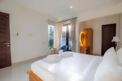 a white bedroom with a large white bed and a chair at Cherish Villa Umalas in Canggu