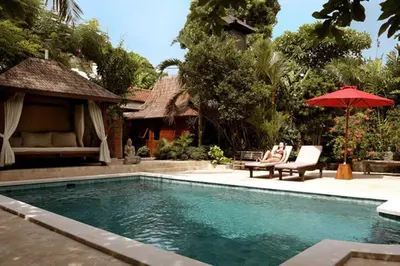 a swimming pool with two chairs and an umbrella at Villa Varuna in Legian