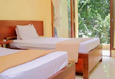two beds in a room with a window at Hotel Damai in Denpasar