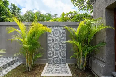a garden with two palm trees next to a wall at Aster Villa by iBali Management in Legian